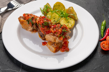stewed pieces of meat with spices. With baked new potatoes and tomato salsa sauce on a white platter and dark background. Dish for the restaurant menu