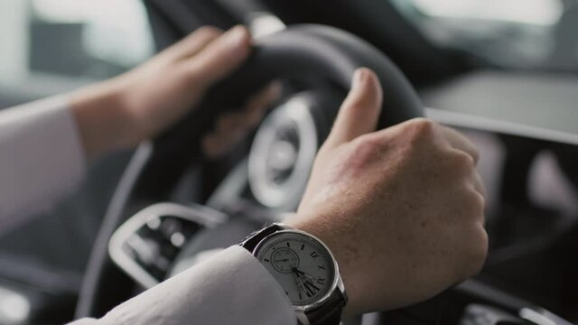 Close up shot of unrecognizable businessman wearing shirt and wristwatch putting his hands on steering wheel of car