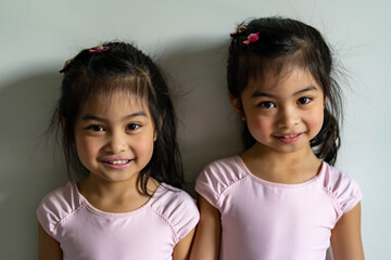 Portrait of cute asian twins smilling on white background wearing pink swim suite or ballet outfit