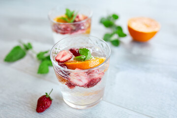 Summer cocktail with strawberry, orange and mint in glass on white table, homemade refreshing lemonade, strawberry punch,copy space.