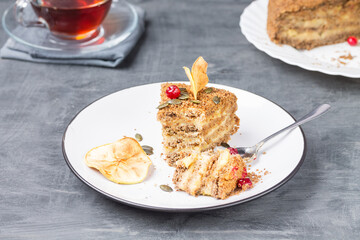 A broken piece of gluten-free nut cake with creamy Apple filling on a plate with a Cup of tea and a large cake in the background.