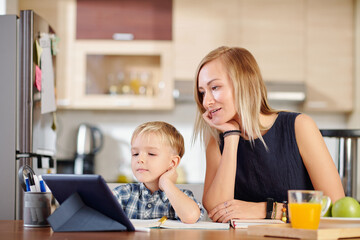 Mother and son watching webinar or online class on tablet computer when sitting at kitchen table at home