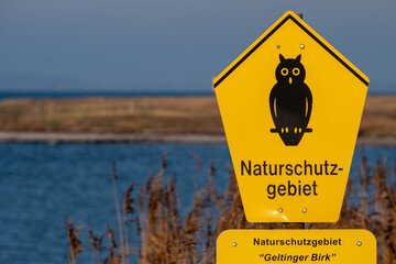 gelbes Schild "Naturschutzgebiet Geltinger Birk" mit Meer im Hintergrund