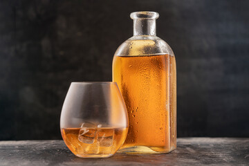 bottle and glass with whiskey or Bourbon Scotch on the table, drops on the glass dark background