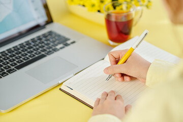 Close-up image of businessman writing thoughts and ideas in planner when working on laptop at office desk