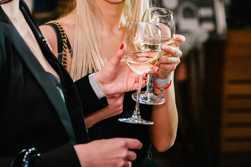 Glasses of wine in the hands of women. Clinking glasses with white wine and toasting.