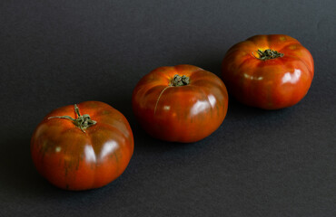 Three tomatoes on a diagonal seen from above on a black background, concept of healthy food
