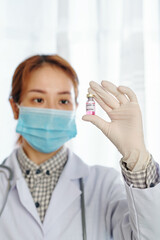 Young serious female physician looking at vial with vaccine against coronavirus in her hand