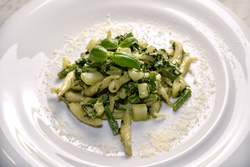 Trofie al pesto - Italian pasta with basil pesto sauce, potatoes and green beans  typical of Genoa, Liguria, Italy - close up in white dish with grated Parmesan cheese
