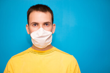 Portrait of tired young man in white medical mask on face for personal protection of coronavirus COVID-19 pandemic isolated on blue background. Exhausted confident person wearing protective face mask.