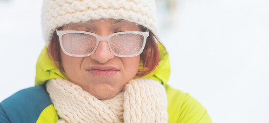 Portrait of a woman in glasses covered with hoarfrost. Upset girl freezing in very cold weather...