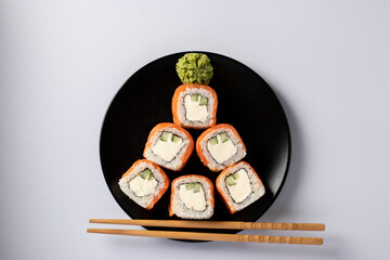 Edible christmas tree made from sushi of salmon with philadelphia cheese on black plate on a white background. New Year party. Top view