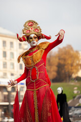 Fototapeta na wymiar Man in a red carnival costume on stilts against the background of the cityscape