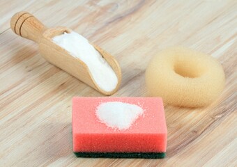 Baking soda (sodium bicarbonate). Soda in a spoon and on the sponge, a scourer and a bowl on the wooden table.  Eco friendly natural cleaners.