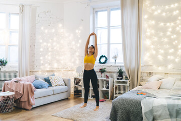 Flexible female yogi practicing hatha at rug stretching body muscles for keeping perfect slim figure, Caucasian fit girl enjoying harmony inspiration during pilates training in cosy home interior