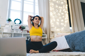 Energetic slim woman in tracksuit stretching and exercising during morning yoga practice in home interior, flexible female gymnastic enjoying pilates time during physical recreation in apartment