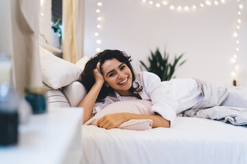 Portrait of cheerful hipster girl with sincerely smile on face looking at camera after morning wake up in comfy home apartment, happy Caucasian woman in sleepclothes enjoying lazy day on weekend