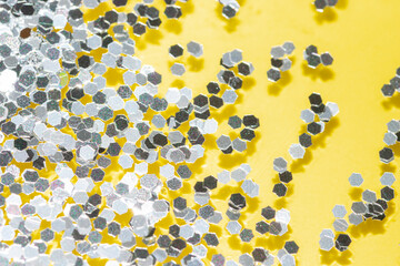 transparent liquid with silver glitter pouring over a pastel yellow background