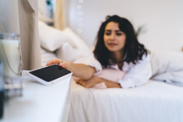 Blurred female checking time on blank smartphone gadget with copy space area for text advertising using home internet connection in bedroom, woman turn off mobile alarm during lazy weekend day