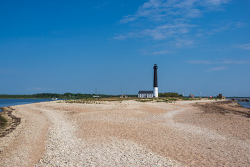 Fototapeta na wymiar View to the beach of Sõrve peninsula cape with sand and pebbles by coastline. Lighthouse in the background. Focus on foreground 