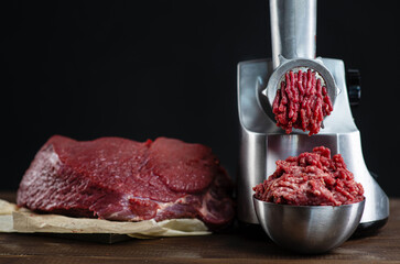 The meat is put in the meat grinder and minced  comes out of it, next to it lies a huge piece of...