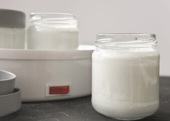 homemade organic yogurt in glass jars near yogurt maker. automatic yogurt machine to make fermented milk product at home. yogurt or kefir making during quarantine concept. 