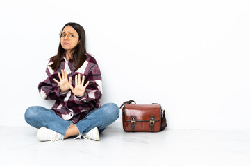 Young student woman sitting on the floor nervous stretching hands to the front