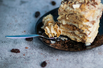 Napolion cake. A piece of cake on a black plate, decorated with raisins. Stands on a table with a gray background
