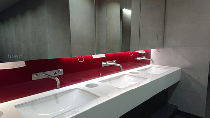 View of the public toilet. White washbasins with metal cranes and mirrors above them.