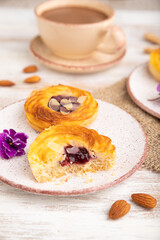 Small cheesecakes with jam and almonds with cup of coffee on a white wooden background. Side view, selective focus.