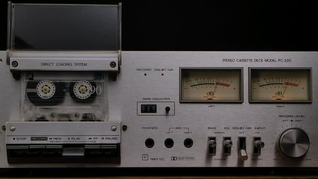Vintage cassette player deck from 80s. Stereo recorder with rotating cassette, controls, dashboard and buttons on black studio background. Close up. Slow motion.