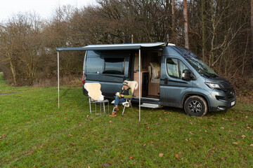 Frau sitzt vor Wohnmobil und liest ein Buch 