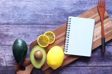 Notepad on chopping board with lime and avocado on table.