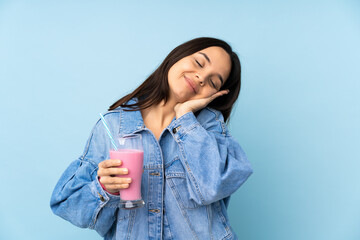 Young woman with strawberry milkshake over isolated blue background making sleep gesture in dorable expression