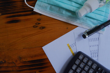 A top view of a facemask, calculator, pen, hand sanitizer, and papers laying on the table