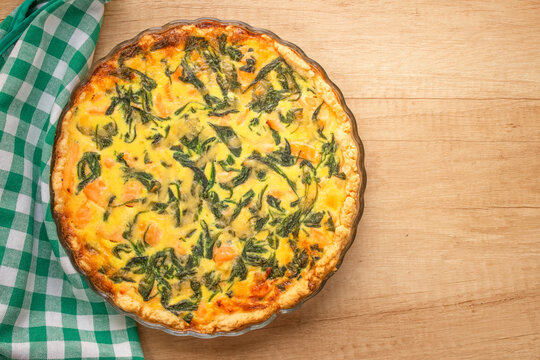 Top view on seafood and salmon fish quiche pie with baby spinach leaves- homemade recipe pie on wooden table background with copy space. Selective focus