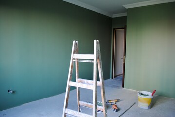 Room in renovation in a nice apartment for relocation with newly dark green painted wall and paint bucket, gloves and spatula on the floor. 