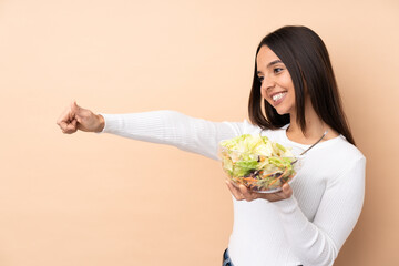 Young brunette girl holding a salad over isolated background giving a thumbs up gesture