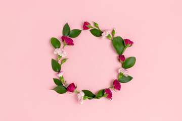 Wreath made of roses, carnation flowers and green leaves on a pink pastel background. Holiday concept with place for text.