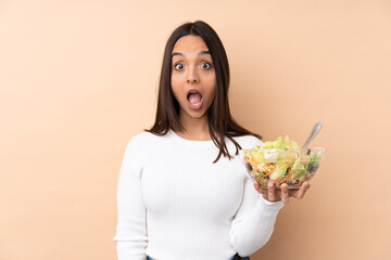 Young brunette girl holding a salad over isolated background with surprise facial expression