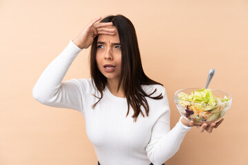 Young brunette girl holding a salad over isolated background looking far away with hand to look something