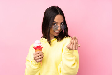 Young brunette girl holding a cornet ice cream over isolated pink background inviting to come with hand. Happy that you came