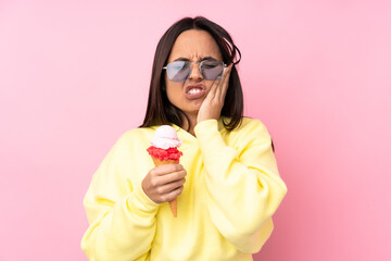 Young brunette girl holding a cornet ice cream over isolated pink background with toothache