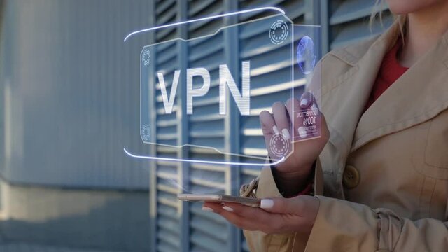 Unrecognizable businesswoman interacts HUD hologram with text VPN. Woman in the coat uses the technology of the future mobile screen on the background of the city