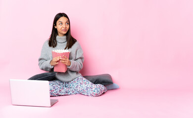 Young mixed race woman eating popcorn while watching a movie on the laptop scheming something