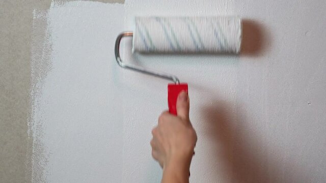woman with painting roller and white paint coloring drywall
