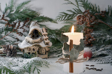 Christmas decoration with candle, house and fir branches. The concept of warmth and comfort in the house for Christmas