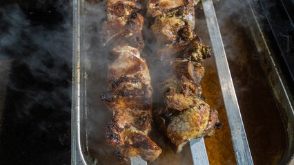 Kebabs threaded on skewers roasted on the grill on the dark background. Defocused smoke on the foreground. Street food concept.