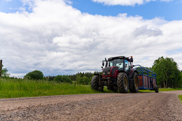 Tractor And Trailer standing near the road in farm during harvesting work in summer under sky with clouds near forest