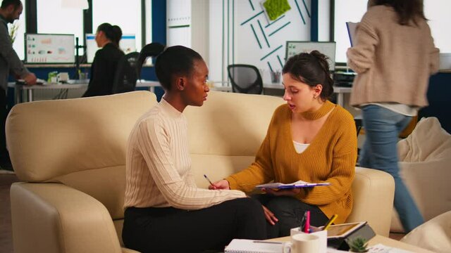 Young diverse woman holding paper document, discussing contract with confident partner in casual wear, signing investment papers. Businesswomen shaking hands, making satisfactorily agreement.